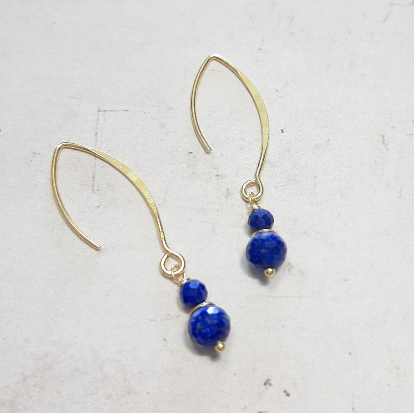 Boucles d’oreilles longues en argent 925 doré, mesurant 4,5 cm de longueur. Rehaussées de pierres naturelles de lapis lazuli, avec des diamètres de 4 mm et 6 mm, offrant des nuances de bleu profond. Les couleurs des pierres peuvent légèrement varier en raison de leur nature authentique, ajoutant une touche unique à chaque bijou.