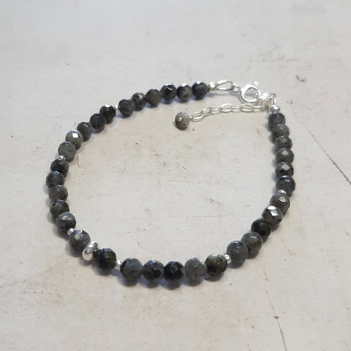 bracelet minimaliste en argent 925, rehaussé par une labradorite noire, également connue sous le nom de larvikite. Mesurant 17 cm, ajustable grâce à une délicate chainette, ce bijou met en valeur une pierre fine de 4 mm de diamètre.