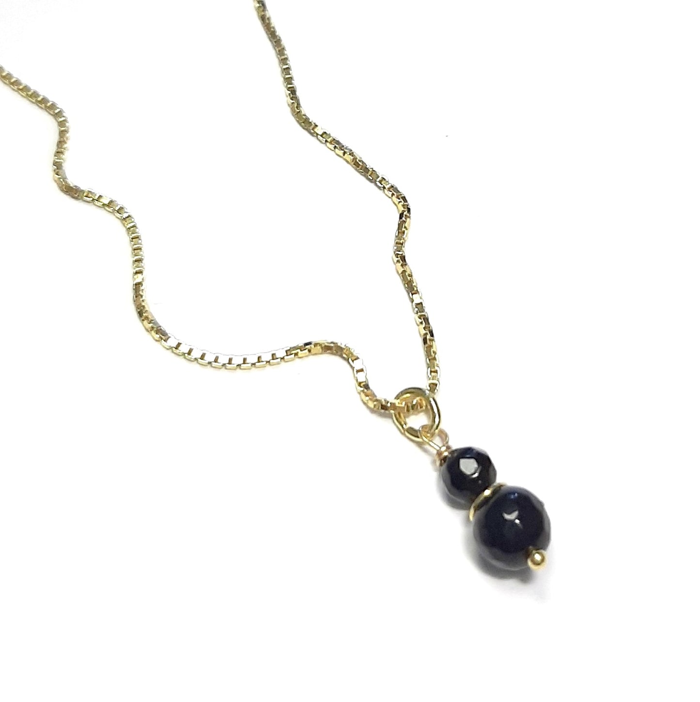 Photo studio du Collier Talisman Onyx, posé à plat sur un fond clair pour montrer l'éclat de l'argent doré.