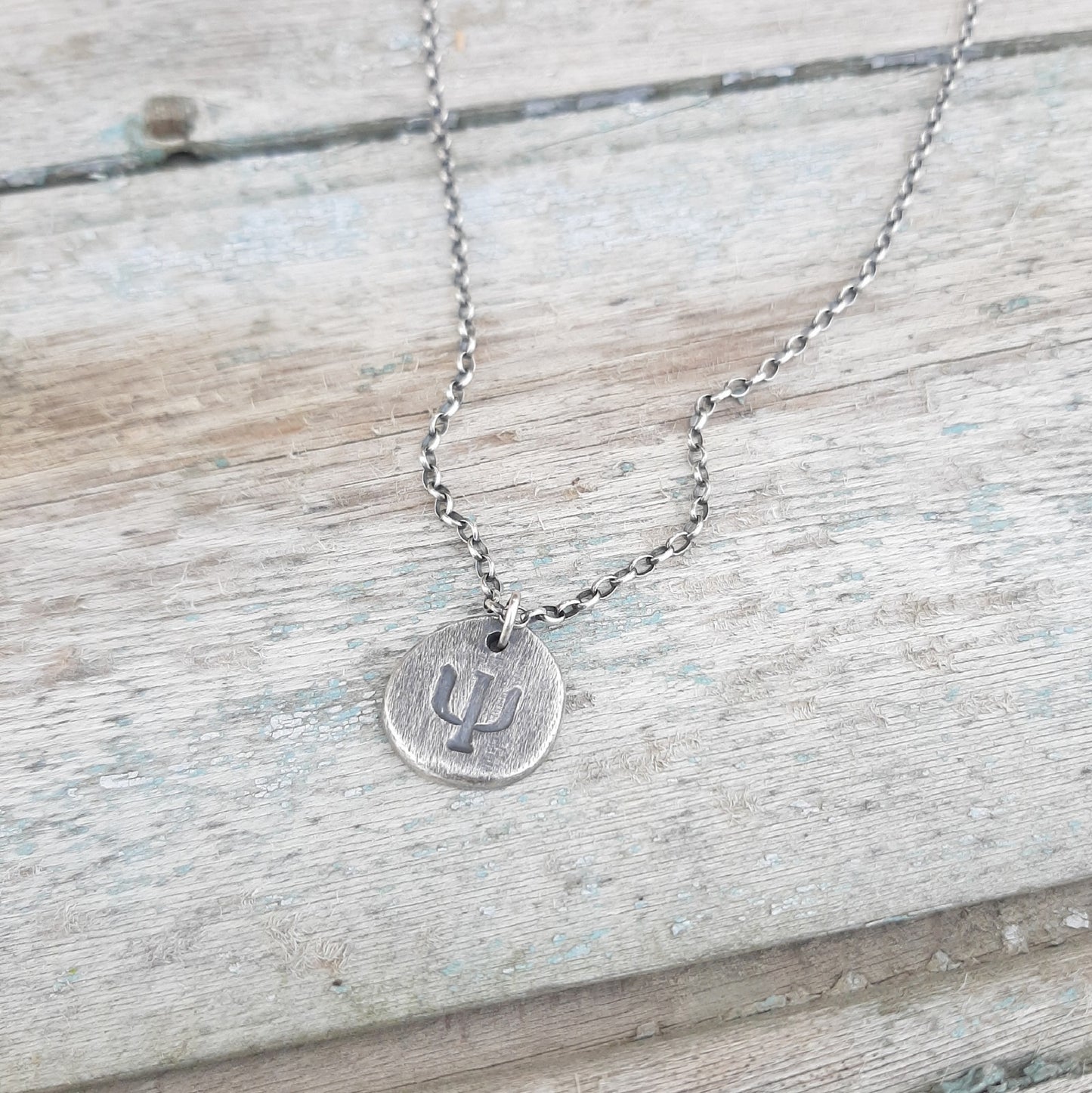 collier ethnique mixte en argent 925 patiné, orné d’un pendentif finement gravé du symbole Psi Ψ, emblème de la psychologie et de l’exploration de l’esprit. Chaque pièce est entièrement façonnée à la main, conférant à votre bijou une authenticité et une singularité incomparables.