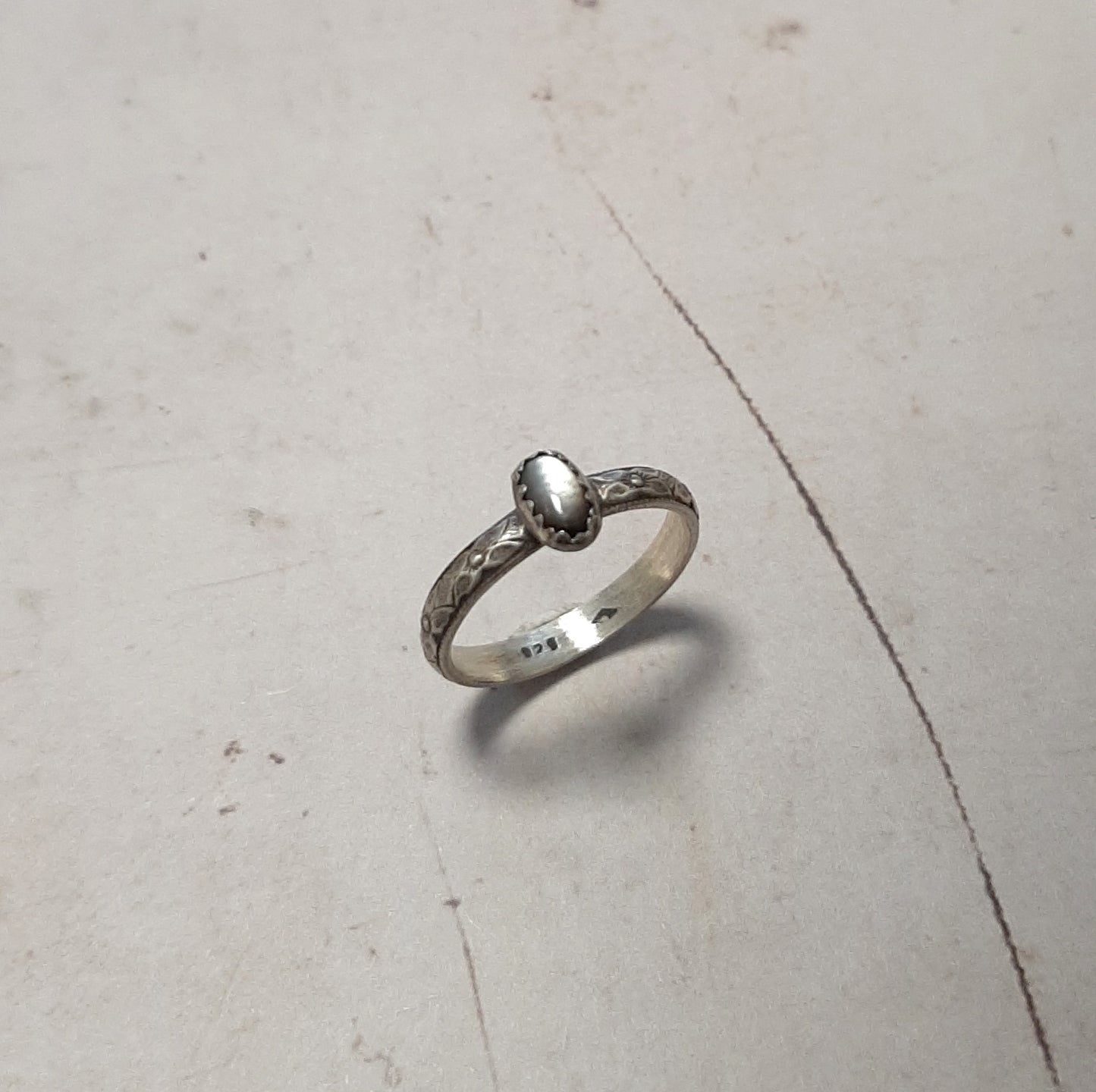 Façonnée en argent massif patiné, cette bague incarne l'art de l'artisanat. La nacre perlière naturelle, capturant la lumière avec ses reflets irisés, confère à cette pièce une élégance singulière. Les motifs floraux sculptés ajoutent une dimension bohème-chic, idéale pour les esprits libres et les amateurs de bijoux authentiques.