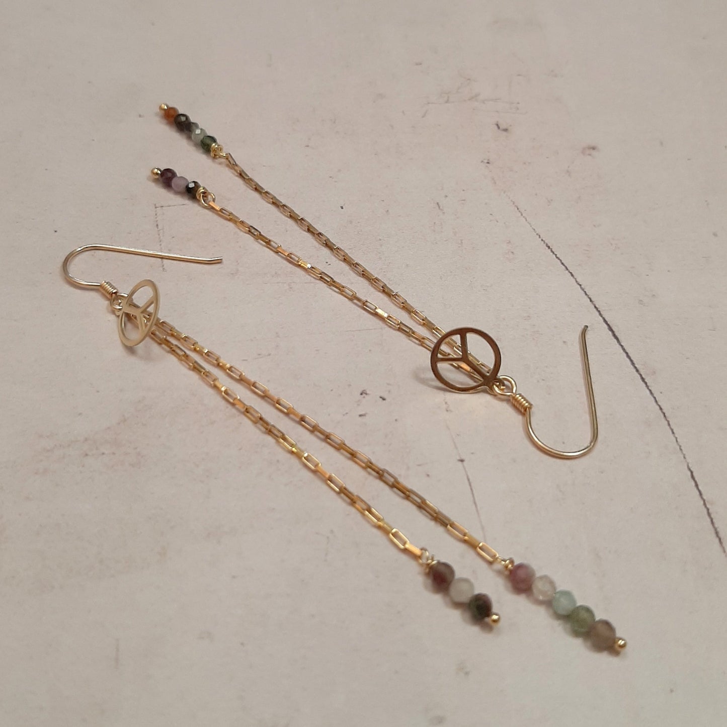 Ces boucles d'oreilles longues sont fabriquées à la main avec de l'argent 925 doré et des pierres naturelles de tourmaline. Elles sont ornées d'une médaille de la paix. Ce bijou bohème est unique et élégant. Il est parfait pour offrir ou pour se faire plaisir.