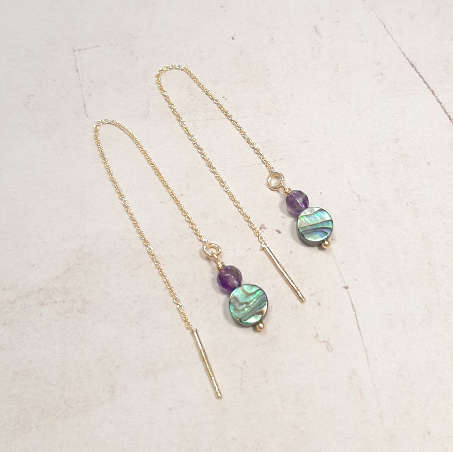 Boucles d'oreilles pendantes en argent 925, agrémentées d'une chaînette délicate et de pierres naturelles d’améthyste et abalone (coquillage). Sans fermoirs, ajustables en glissant la chaîne directement dans le lobe de l'oreille, permettant de choisir la longueur souhaitée. boucles d'oreilles pendantes, argent 925, pierres naturelles, améthyste, abalone, bijoux ajustables, chaînette délicate, bijoux sans fermoirs, boucles d'oreilles modernes, design élégant.