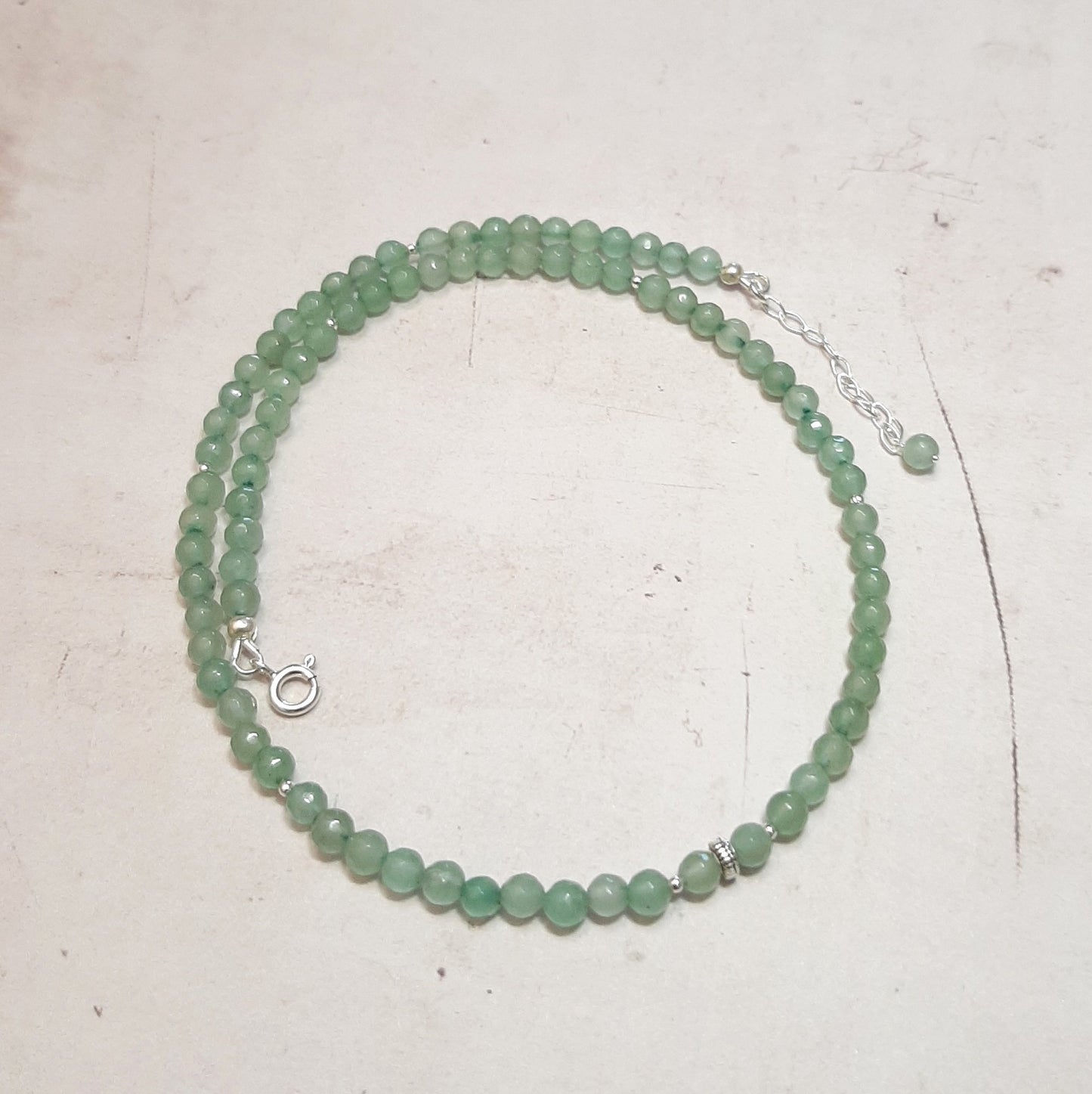 Collier ras-du-cou en argent 925, orné de pierres naturelles d'aventurine verte. Conçu pour transcender les tendances éphémères, ce bijou intemporel s'adapte à tous les genres. Mesurant 40 cm avec une chaînette supplémentaire, il présente des perles d'aventurine de 4 mm de diamètre. L'aventurine verte est reconnue pour ses effets antistress, sa capacité à rendre patient et à calmer la colère.