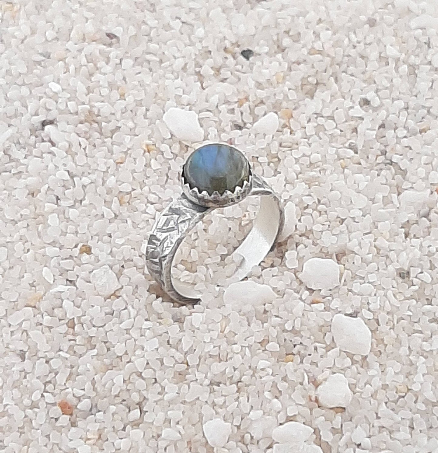Bague ethnique en argent massif ornée d'un cabochon de labradorite naturelle de 8 mm. La largeur de l'anneau est de 4 mm. Chaque bijou est façonné à la main, avec des variations subtiles qui rendent chaque pièce unique. La labradorite est connue pour ses propriétés protectrices, formant un bouclier contre les énergies négatives tout en préservant l'énergie personnelle. Idéale pour ceux en quête d'un bijou à la fois esthétique et spirituel.