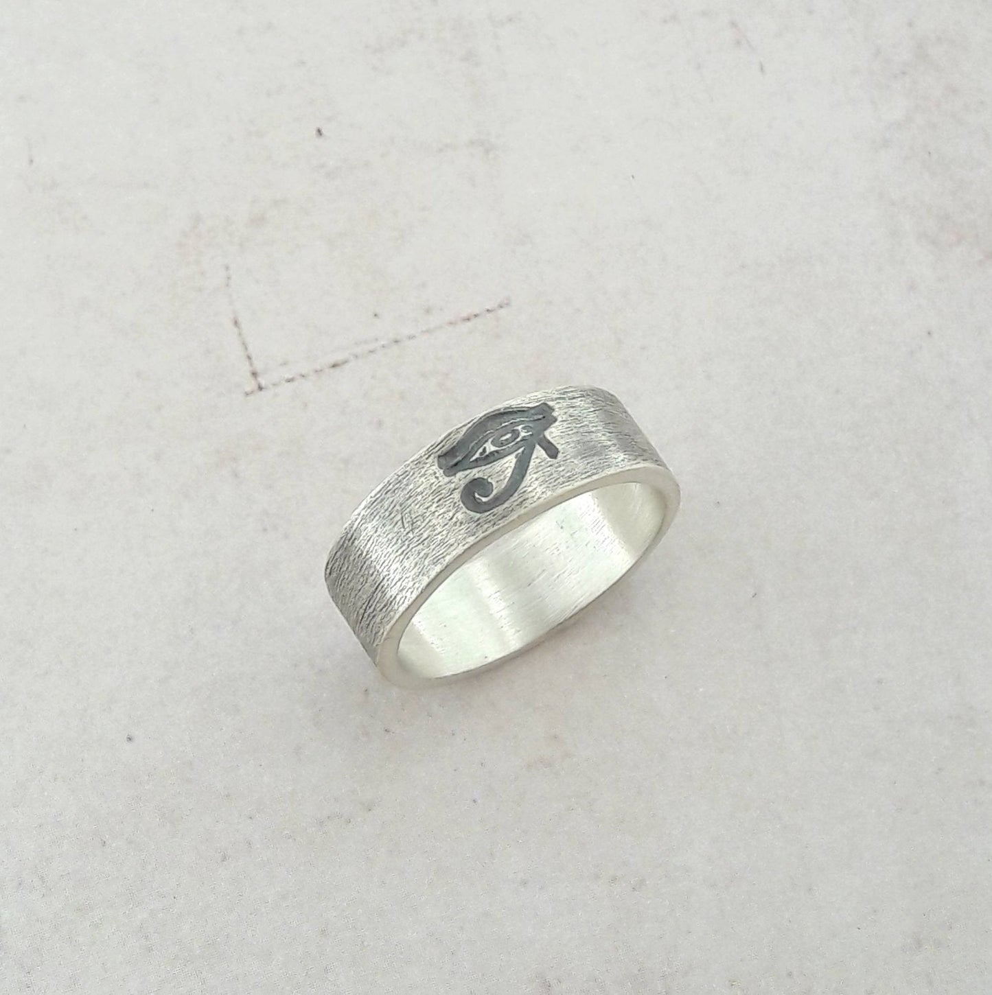 La bague "Œil d'Horus" en argent massif patiné, avec une largeur d'environ 6 mm, se distingue par son design symbolique et intemporel. Unisexe, elle convient aussi bien aux hommes qu'aux femmes. L’Œil d’Horus, également appelé oudjat, est un symbole ancien de protection et de clairvoyance, souvent porté comme un porte-bonheur. Fabriquée sur commande, elle est expédiée sous un délai de 5 jours, garantissant une pièce unique et personnelle. Idéale pour enrichir un style avec une touche d’exotisme et d’histoir