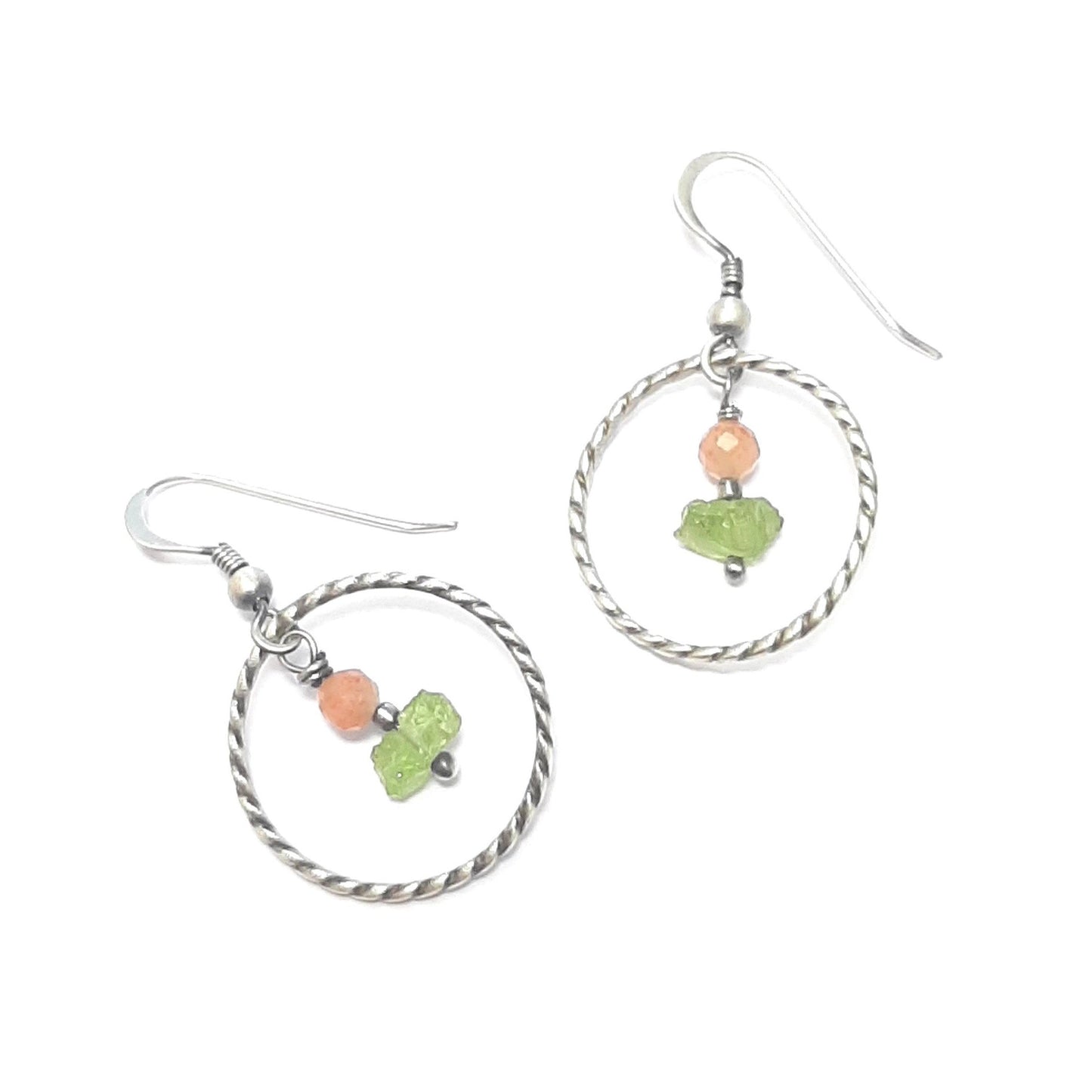 Les boucles d'oreilles ethniques en argent massif patiné sont sublimées par des pierres naturelles de pierre de soleil et de péridot. Chaque pierre étant unique, les couleurs et les formes varient, ajoutant une touche personnalisée à chaque pièce. La longueur totale est de 3,8 cm, avec un diamètre de cercle de 21 mm.