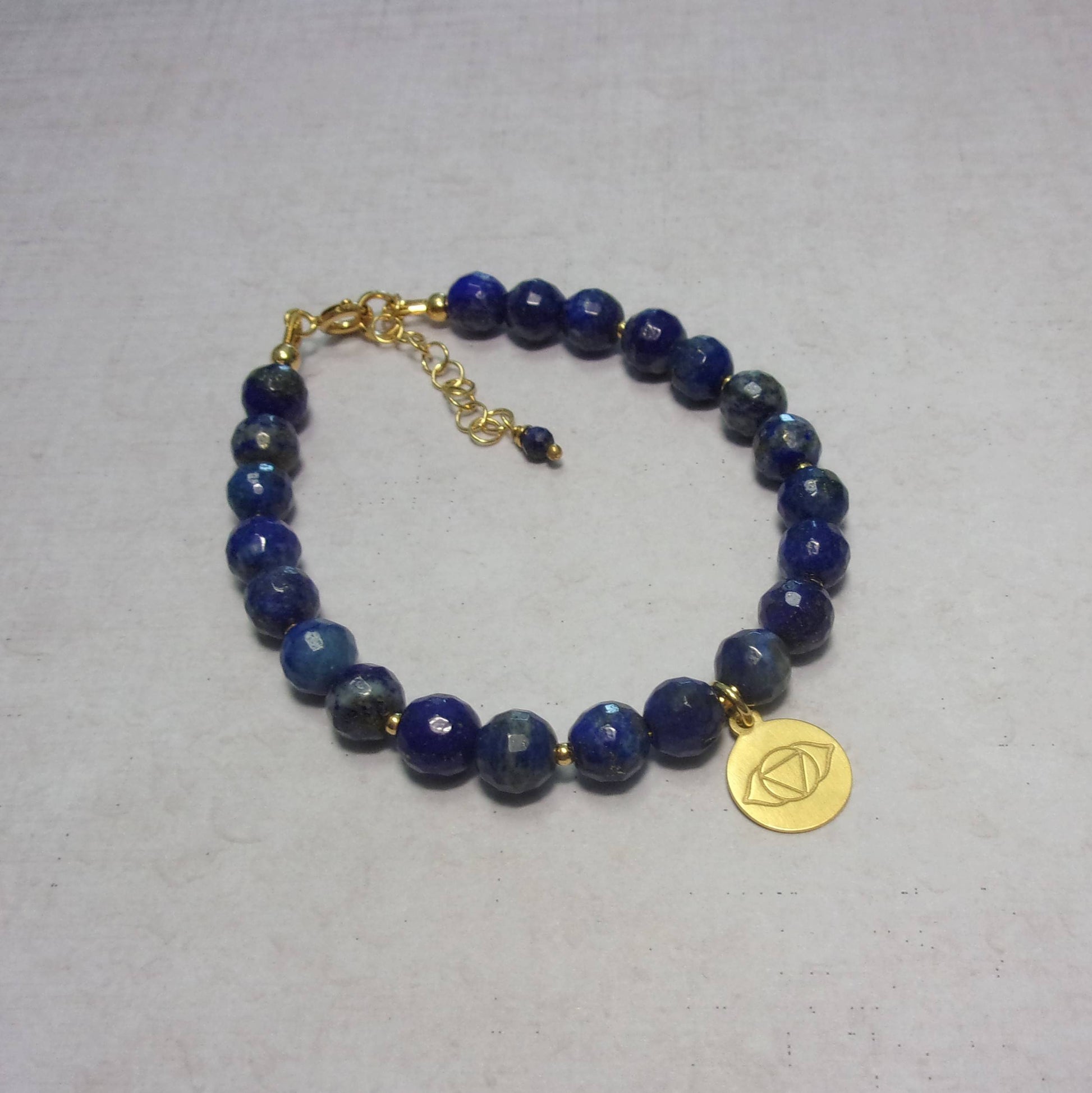 Ce bracelet en lapis-lazuli, orné d'une délicate médaille représentant le chakra Ajna, comprend des apprêts en argent 925 doré. Mesurant 17 cm de longueur, avec une chaînette supplémentaire, le bracelet présente des perles de lapis-lazuli de 6 mm de diamètre.