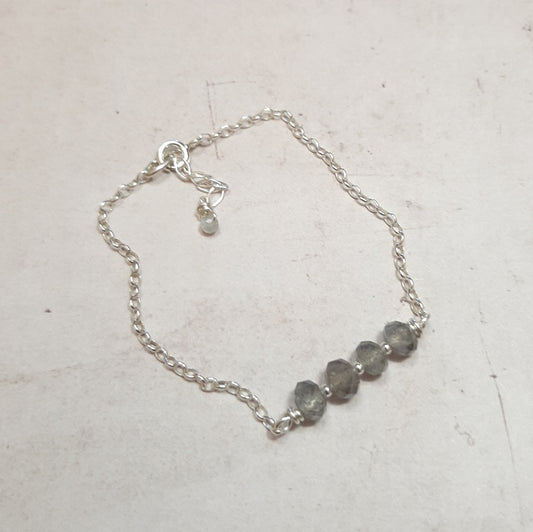 Un bracelet délicat de 17 cm, complété par une chaînette pour un ajustement sur-mesure. Confectionné en argent 925, il est orné de pierres naturelles facettées de labradorite, dont les nuances peuvent légèrement varier, offrant une touche unique à chaque pièce. La labradorite, reconnue pour ses propriétés protectrices, agit comme un bouclier, absorbant les énergies négatives, les maux et les chagrins. Ce bracelet combine protection et élégance, parfait pour un usage quotidien ou pour des occasions spéciales