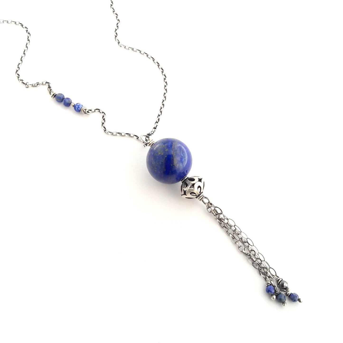 Imaginez un long cordon souple en argent 925, d'une longueur de 90 centimètres. À l'une des extrémités, ce cordon soutient un pendentif rond en lapis-lazuli. Cette pierre naturelle présente une couleur bleue intense, parsemée parfois de petites veines dorées. Le toucher du métal argenté et la douceur de la pierre créent une sensation agréable au contact de la peau.