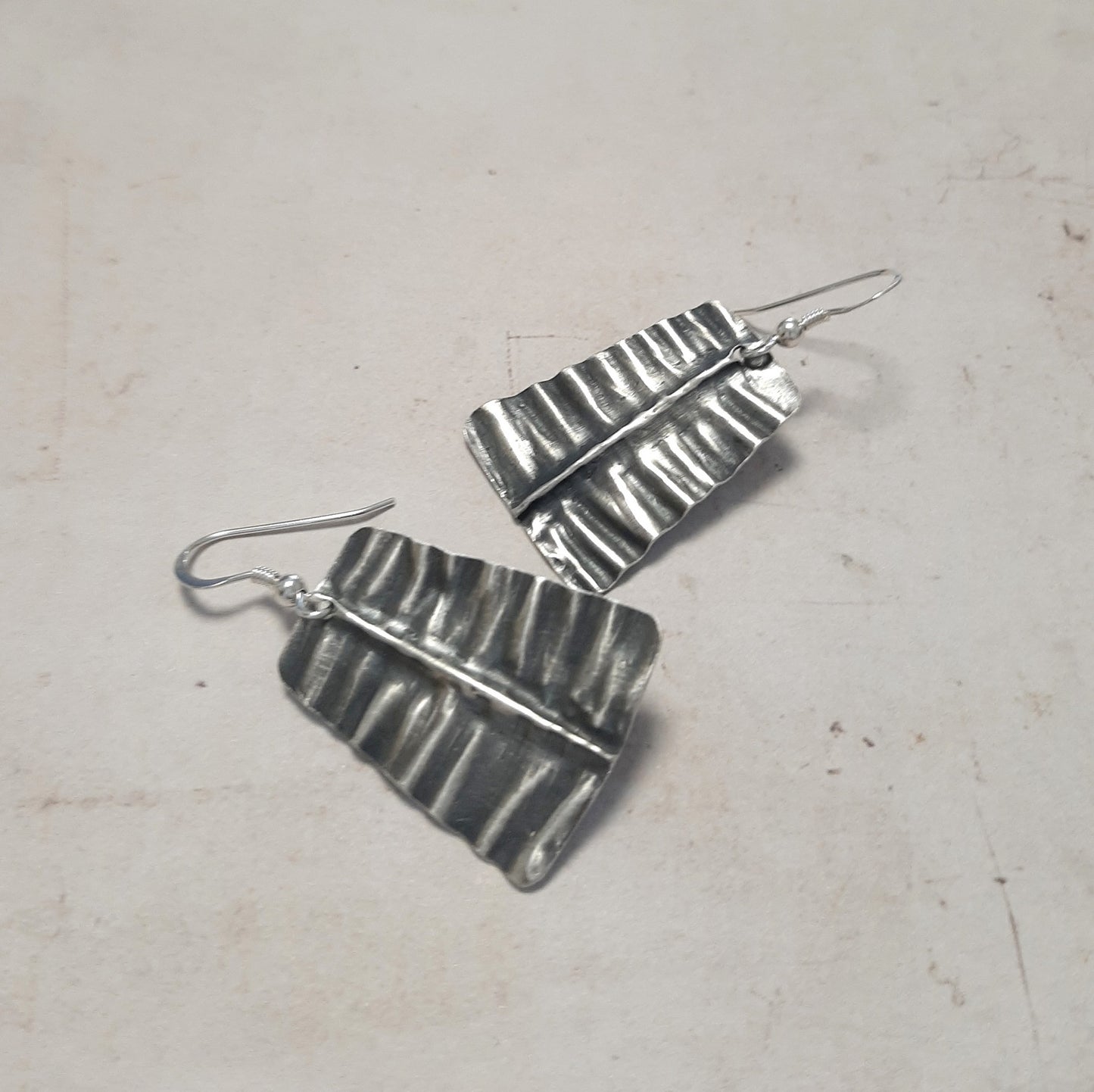 Boucles d'oreilles en argent massif, délicatement martelées et patinées pour évoquer la texture d'une feuille. Chaque bijou, façonné à la main, présente des petites variations par rapport à la photo