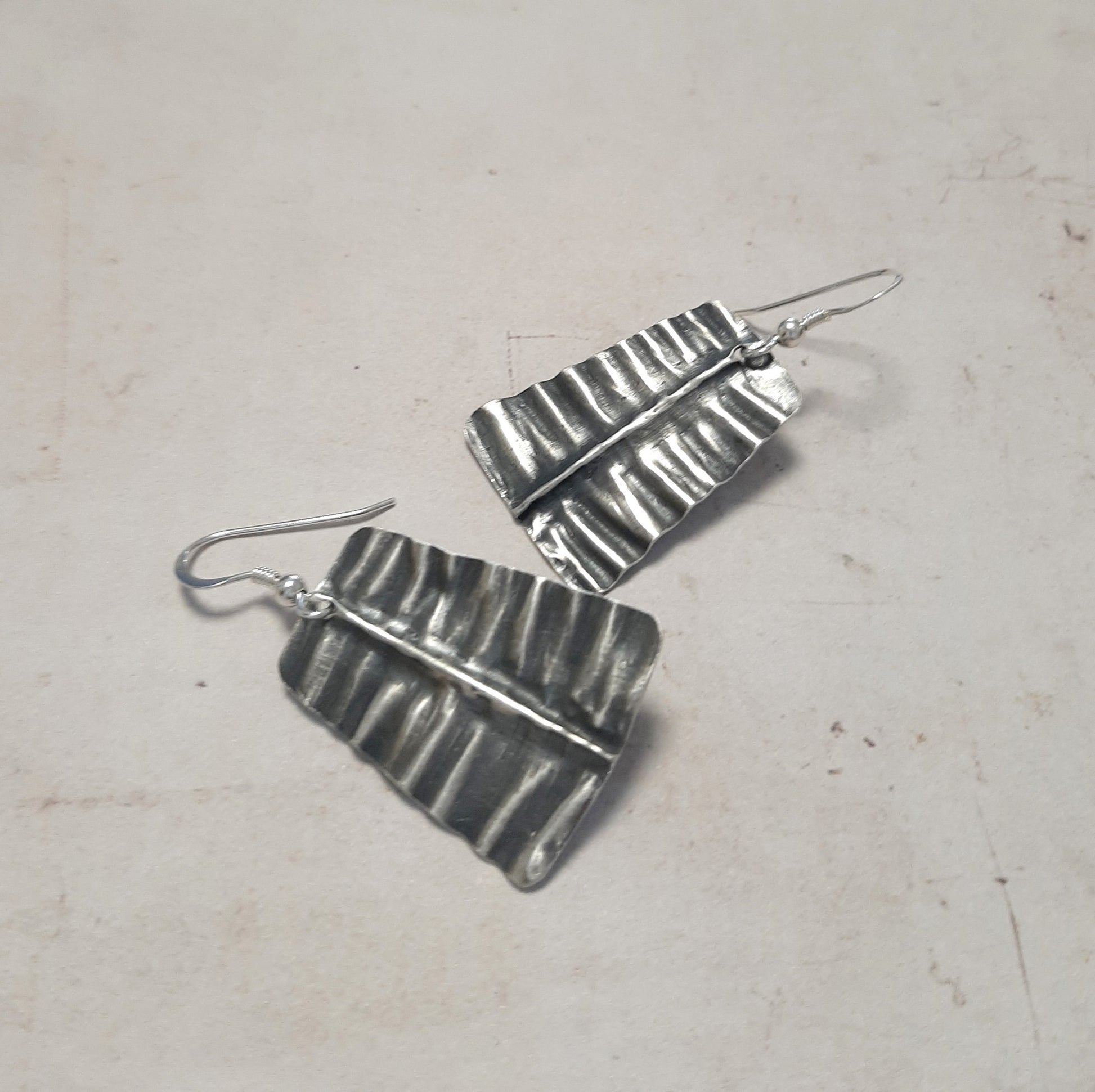 Boucles d'oreilles en argent massif, délicatement martelées et patinées pour évoquer la texture d'une feuille. Chaque bijou, façonné à la main, présente des petites variations par rapport à la photo
