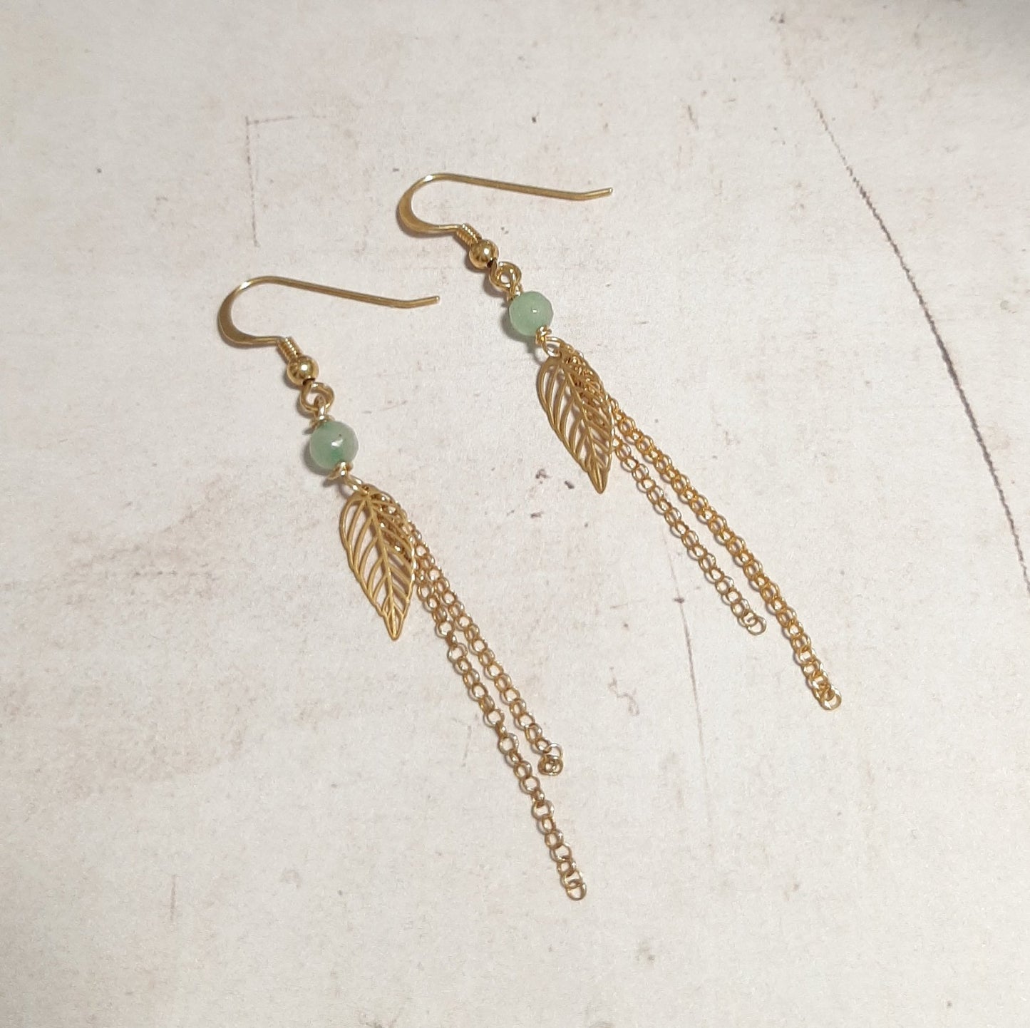 Boucles d’oreilles en argent 925 doré avec chaînes pendantes, ornées d’une feuille et de pierres naturelles d’aventurine verte.  Les pierres naturelles peuvent présenter des variations de couleur, rendant chaque paire unique.  Longueur : 7 cm environ  ✨ L'aventurine verte est associée à la chance et à la prospérité. Elle apporterait aussi calme et équilibre émotionnel.