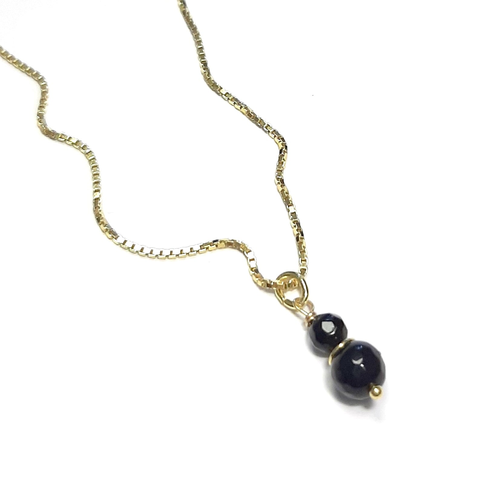 Photo studio du Collier Talisman Onyx, posé à plat sur un fond clair pour montrer l'éclat de l'argent doré.