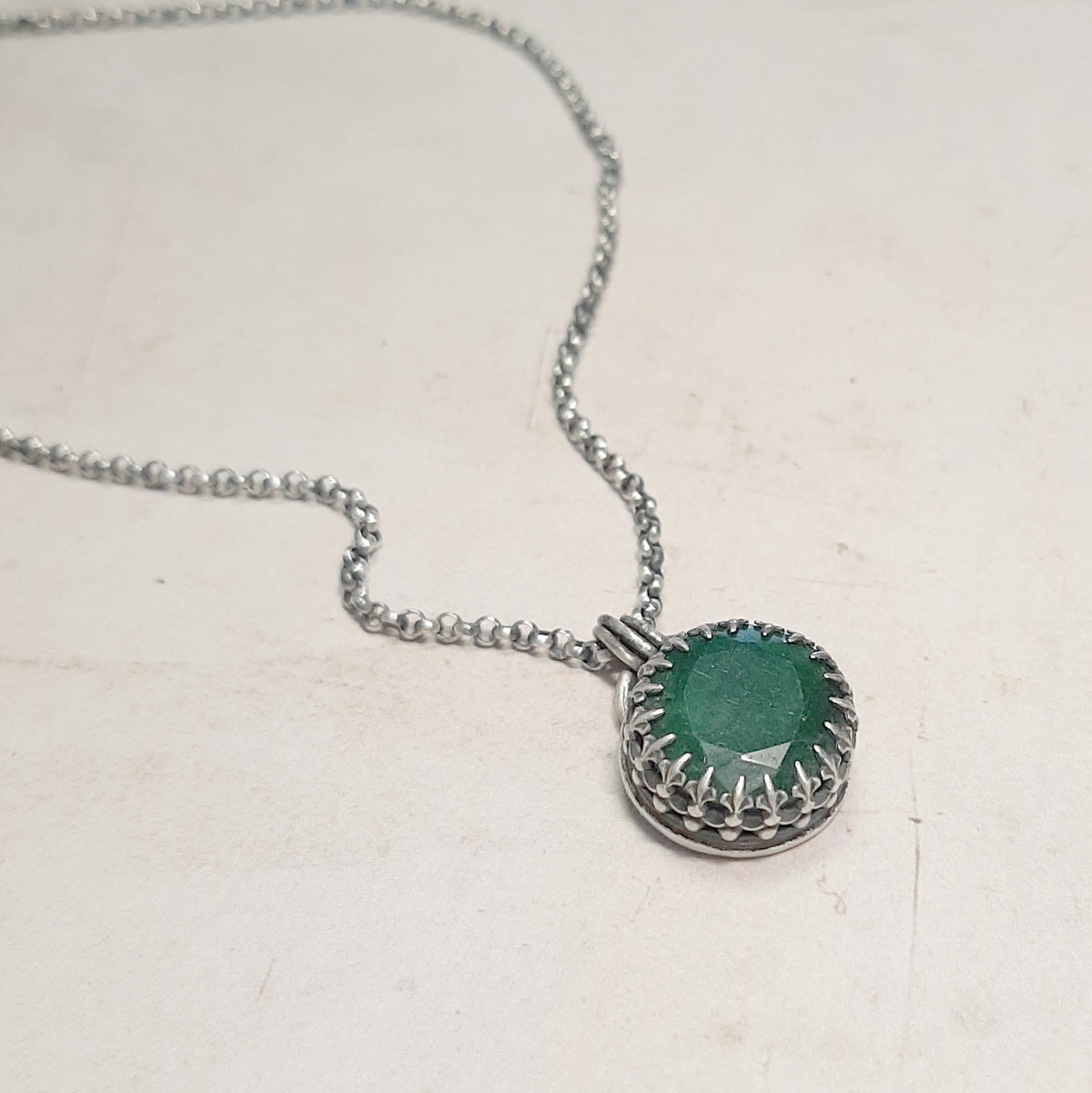 Collier ethnique avec émeraude ovale facettée et monture en argent ajourée, posé sur fond clair.