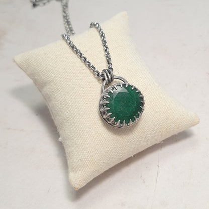  Pendentif en émeraude facettée avec monture  à griffes en argent patiné, présenté sur un coussin écru.