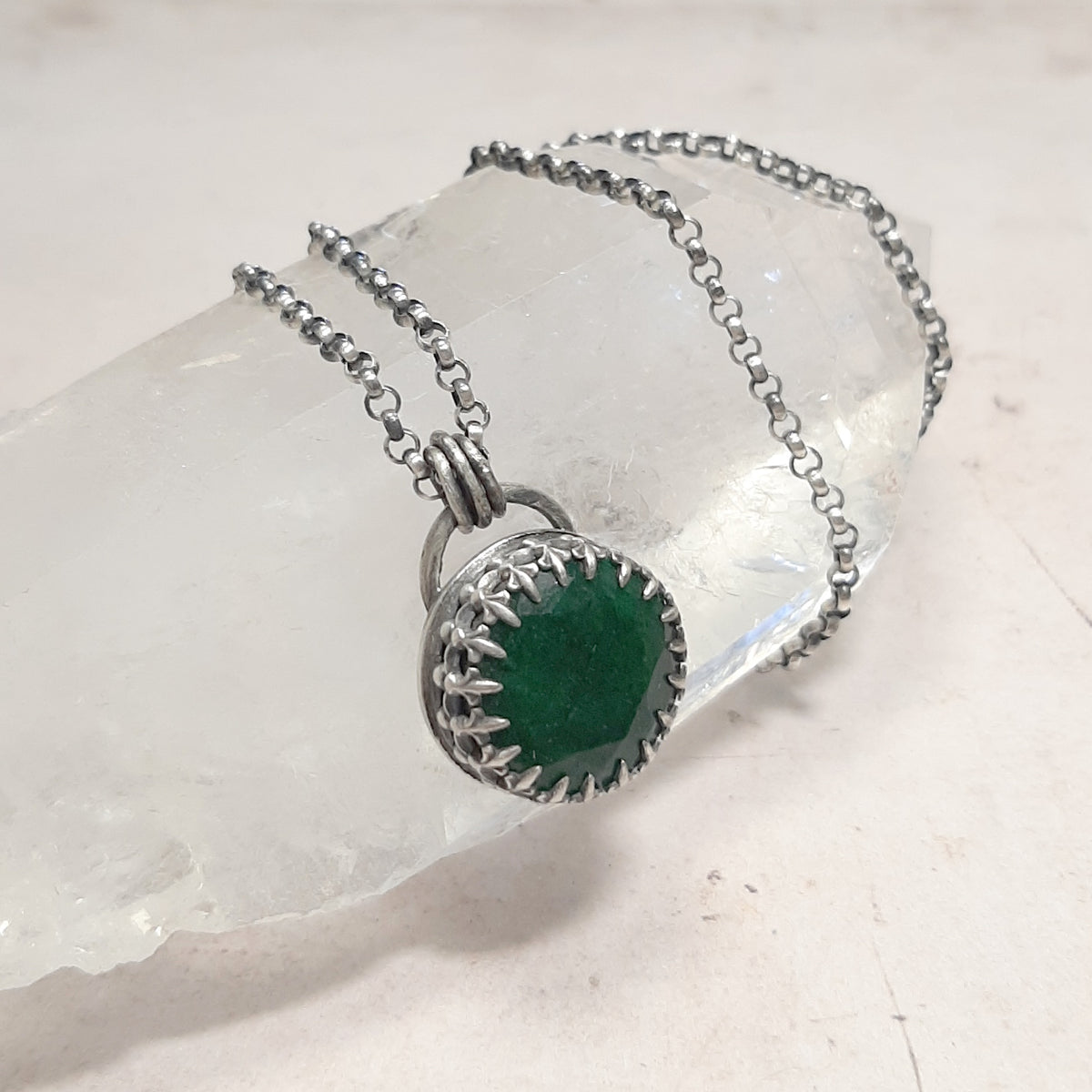 Collier avec pendentif ovale en émeraude verte, monture à griffes et chaîne argentée sur une pierre blanche