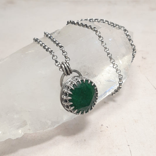 Collier avec pendentif ovale en émeraude verte, monture à griffes et chaîne argentée sur une pierre blanche
