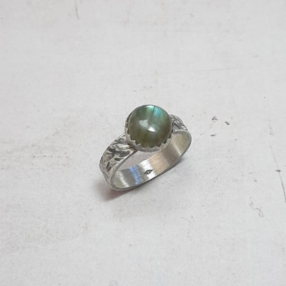 Bague ethnique en argent massif ornée d'un cabochon de labradorite naturelle de 8 mm. La largeur de l'anneau est de 4 mm. Chaque bijou est façonné à la main, avec des variations subtiles qui rendent chaque pièce unique. La labradorite est connue pour ses propriétés protectrices, formant un bouclier contre les énergies négatives tout en préservant l'énergie personnelle. Idéale pour ceux en quête d'un bijou à la fois esthétique et spirituel.