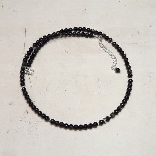 Collier en argent 925 est orné de pierres naturelles d'obsidienne dorée, mesurant 4 mm de diamètre. La longueur du collier est de 40 cm, avec une chaînette supplémentaire. L'obsidienne dorée, une variété d’obsidienne parsemée de fines paillettes dorées, présente des reflets dorés discrets qui varient selon la lumière.