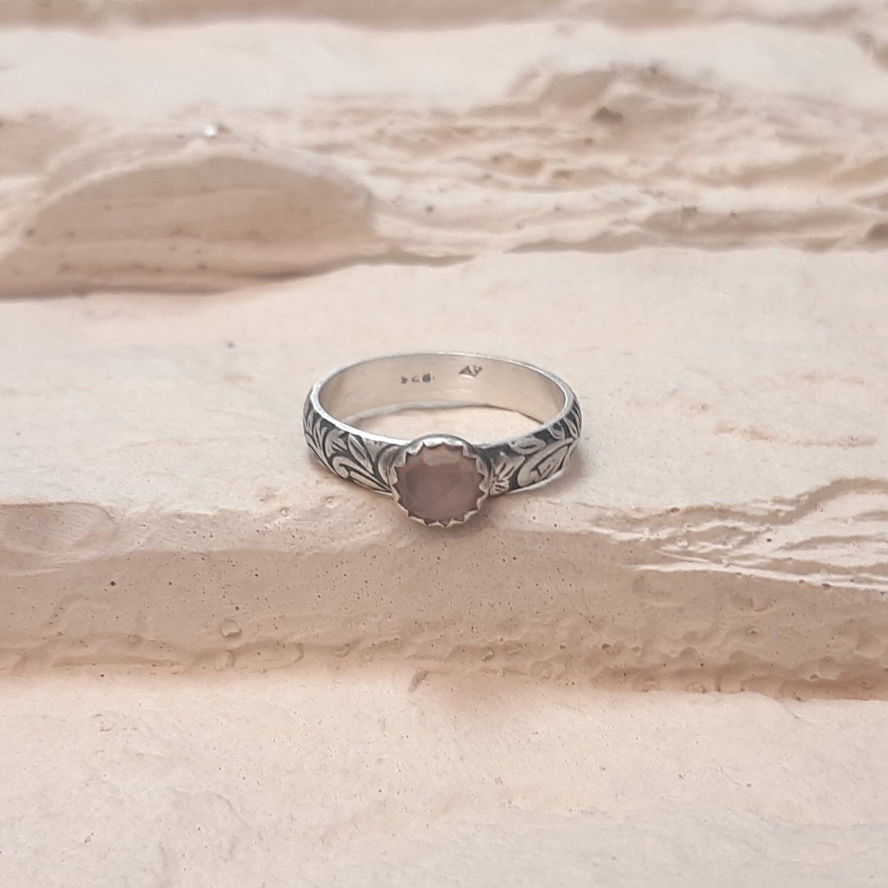 La Bague Calcédoine Rose Tropicália est un bijou artisanal en argent massif, orné d'une pierre naturelle de calcédoine rose. Son design ethnique unique, gravé de motifs floraux et feuillus, incarne à la fois élégance et spiritualité. La calcédoine rose est reconnue pour ses propriétés apaisantes, ce qui en fait un choix idéal pour ceux recherchant harmonie et beauté dans leurs accessoires. Cette bague allie tradition et modernité, parfaite pour les amateurs de bijoux faits main.