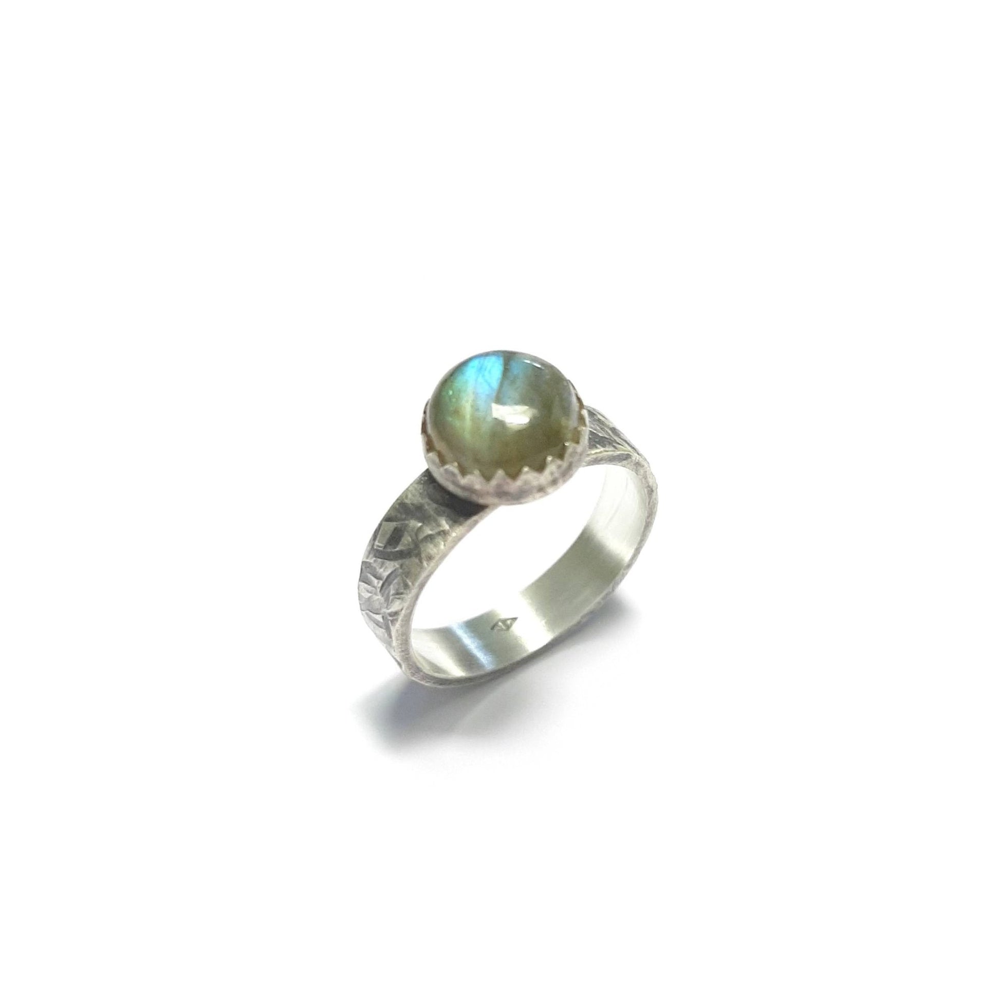 Bague ethnique en argent massif ornée d'un cabochon de labradorite naturelle de 8 mm. La largeur de l'anneau est de 4 mm. Chaque bijou est façonné à la main, avec des variations subtiles qui rendent chaque pièce unique. La labradorite est connue pour ses propriétés protectrices, formant un bouclier contre les énergies négatives tout en préservant l'énergie personnelle. Idéale pour ceux en quête d'un bijou à la fois esthétique et spirituel.