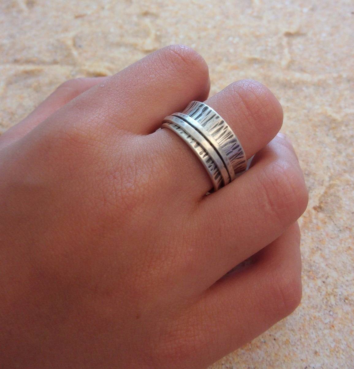 La Bague de Méditation en Argent Massif est un bijou artisanal de 10 mm de large, avec une finition martelée et patinée. Inspirée du moulin à prière tibétain, cette bague anti-stress comporte deux anneaux qui tournent librement autour de l'anneau principal, favorisant la relaxation et la concentration. Idéale pour les moments de méditation ou pour apaiser l'esprit au quotidien, elle allie élégance et fonctionnalité.
