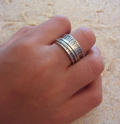 La Bague de Méditation en Argent Massif est un bijou artisanal de 10 mm de large, avec une finition martelée et patinée. Inspirée du moulin à prière tibétain, cette bague anti-stress comporte deux anneaux qui tournent librement autour de l'anneau principal, favorisant la relaxation et la concentration. Idéale pour les moments de méditation ou pour apaiser l'esprit au quotidien, elle allie élégance et fonctionnalité.