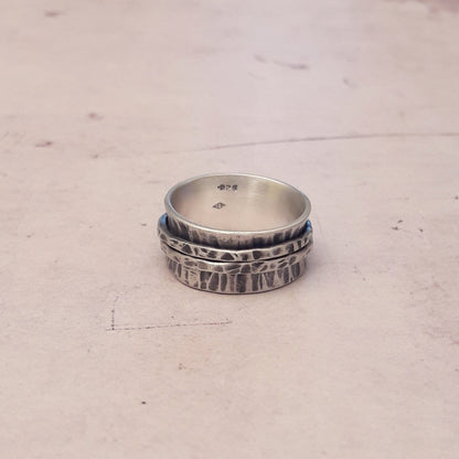 La Bague de Méditation en Argent Massif est un bijou artisanal de 10 mm de large, avec une finition martelée et patinée. Inspirée du moulin à prière tibétain, cette bague anti-stress comporte deux anneaux qui tournent librement autour de l'anneau principal, favorisant la relaxation et la concentration. Idéale pour les moments de méditation ou pour apaiser l'esprit au quotidien, elle allie élégance et fonctionnalité. Bijoux non genrés. Bague anti stress made in france
