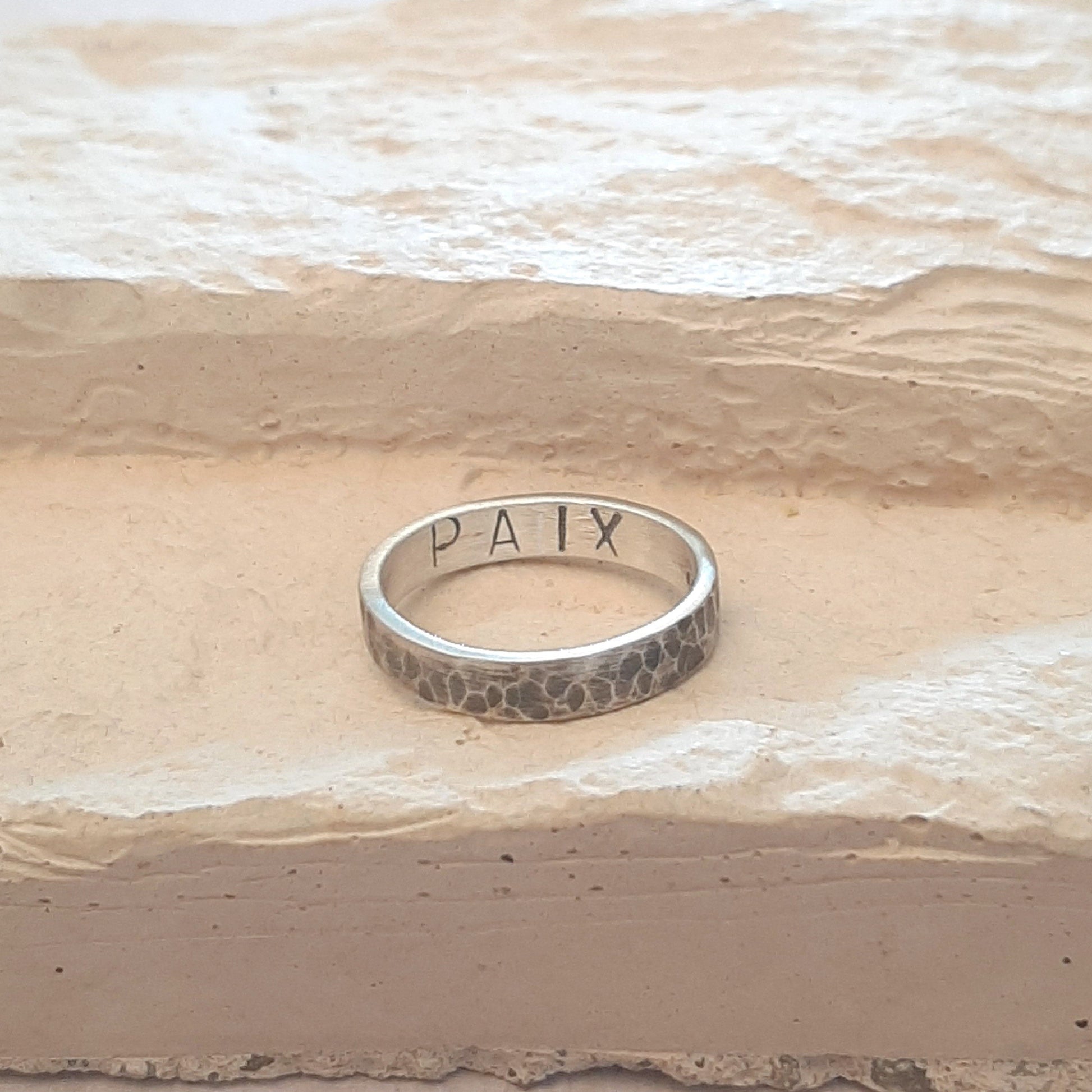 Bague en argent massif martelé et patiné, au design unique et artisanal. L'intérieur de l'anneau présente une gravure personnalisable, jusqu'à 6 caractères, offrant la possibilité d'y inscrire un message, une date ou un prénom. 
Bijoux durables en argent.