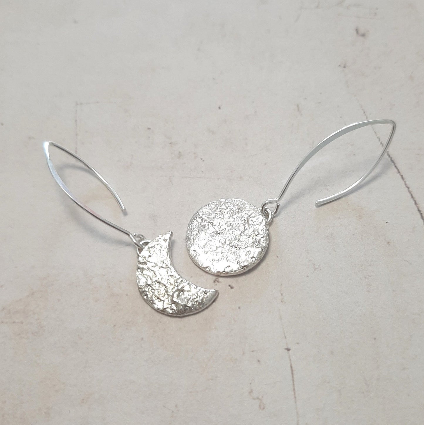 Ces boucles d'oreilles asymétriques en argent massif, inspirées de la mythologie tupi-guarani, représentent un croissant et une pleine lune. Chaque pièce est faite main, avec une texture organique unique. Le design élégant et raffiné rappelle la beauté mystique de Jaci, déesse de la lune.
