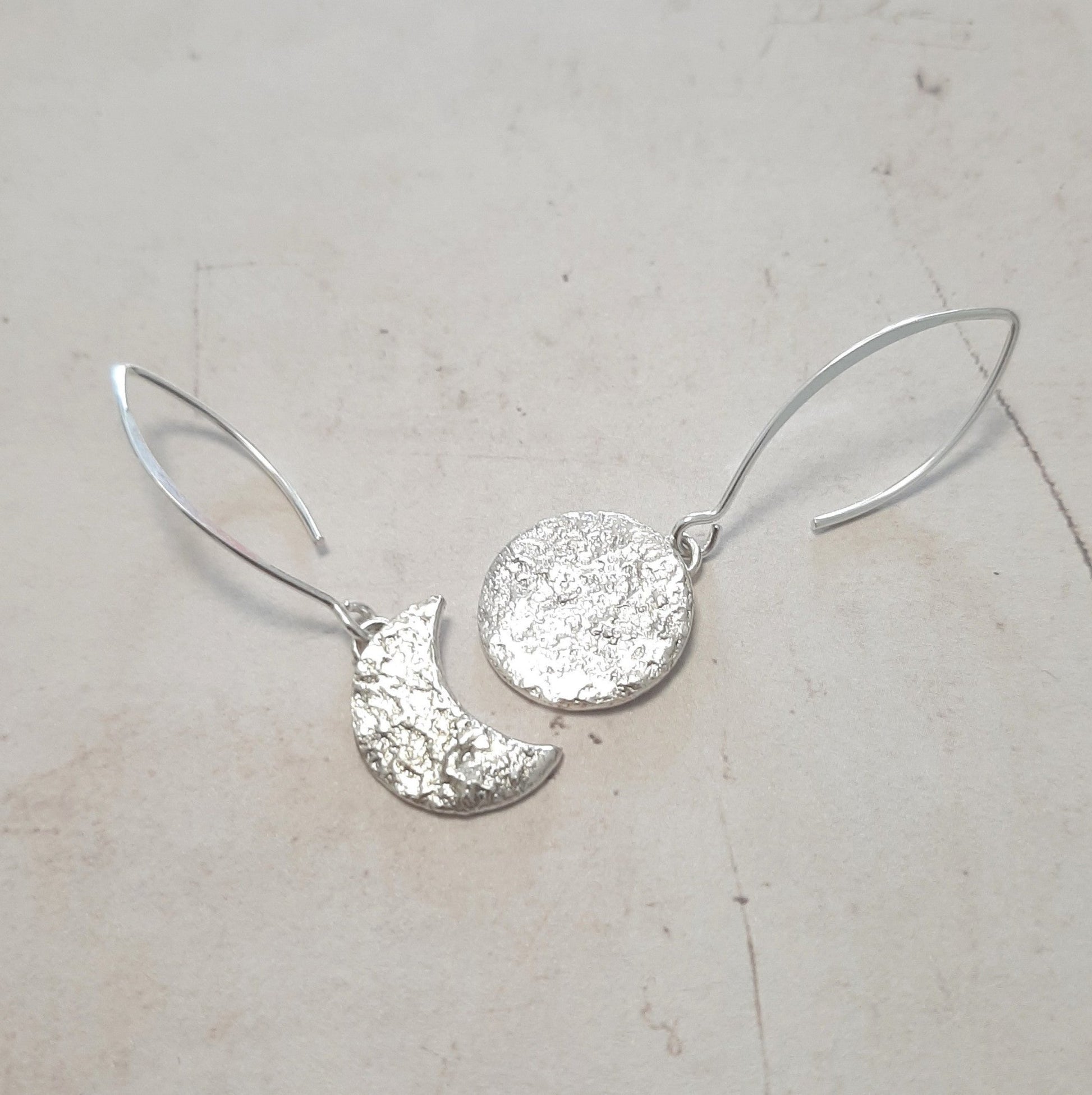 Ces boucles d'oreilles asymétriques en argent massif, inspirées de la mythologie tupi-guarani, représentent un croissant et une pleine lune. Chaque pièce est faite main, avec une texture organique unique. Le design élégant et raffiné rappelle la beauté mystique de Jaci, déesse de la lune.