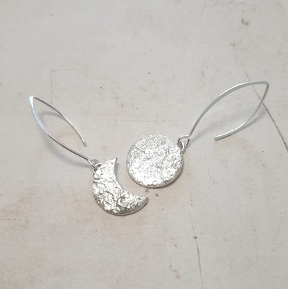 Ces boucles d'oreilles asymétriques en argent massif, inspirées de la mythologie tupi-guarani, représentent un croissant et une pleine lune. Chaque pièce est faite main, avec une texture organique unique. Le design élégant et raffiné rappelle la beauté mystique de Jaci, déesse de la lune.
