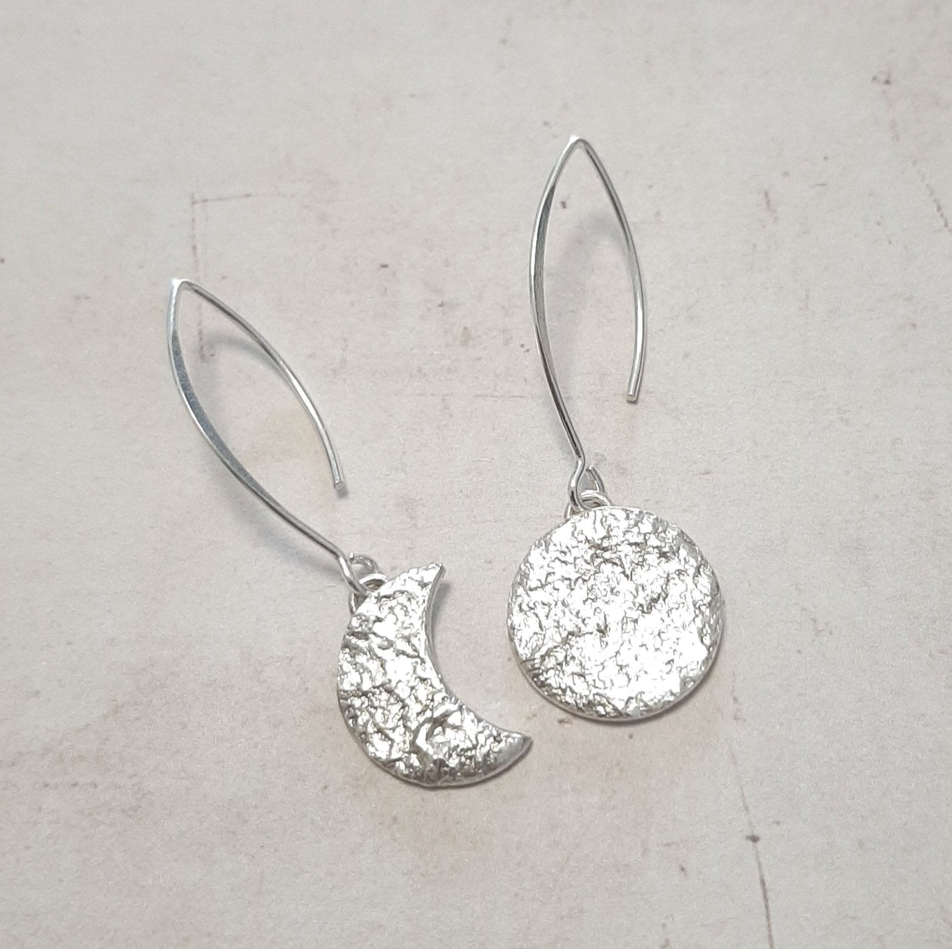 Ces boucles d'oreilles asymétriques en argent massif, inspirées de la mythologie tupi-guarani, représentent un croissant et une pleine lune. Chaque pièce est faite main, avec une texture organique unique. Le design élégant et raffiné rappelle la beauté mystique de Jaci, déesse de la lune.