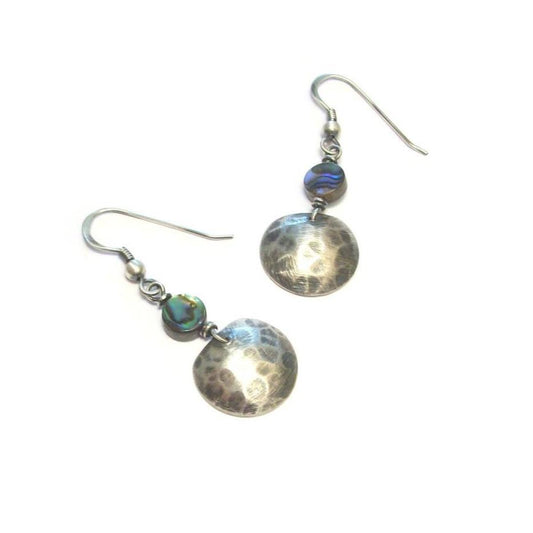 Boucles d'oreilles ethniques en argent massif 925 patiné noir, soigneusement martelé à la main et ornées d'abalone naturelle. La longueur totale atteint 4,1 cm, offrant une présence délicate et raffinée. L'abalone, ou ormeau, est un mollusque marin prisé pour sa coquille aux reflets irisés et couleurs éclatantes, allant du bleu au vert, en passant par le violet et le rose. 