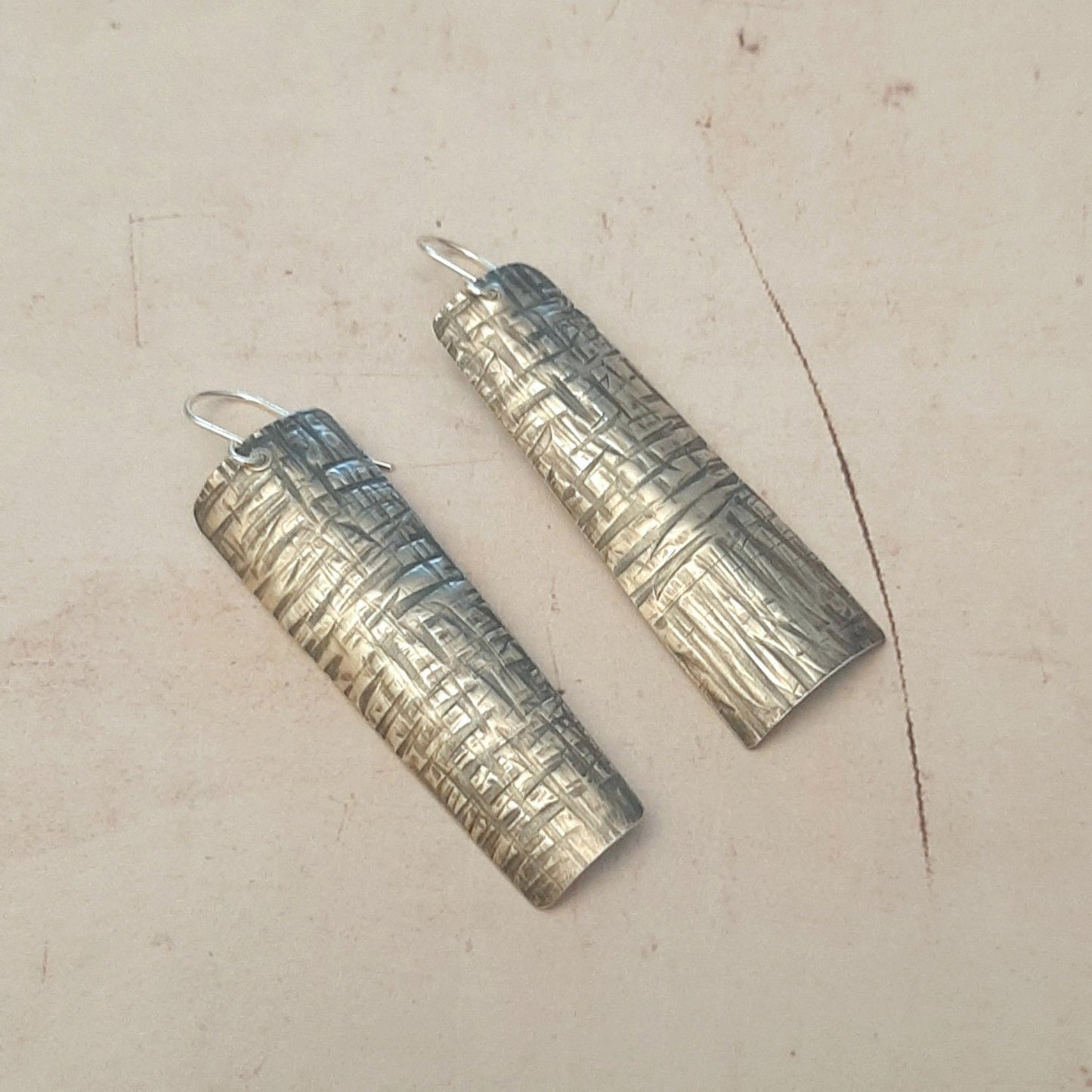 Boucles d'oreilles longues ethniques en argent massif martelé, légèrement asymétriques. Les reliefs, révélés par la patine, évoquent le tronc du "tucum", palmier tropical.