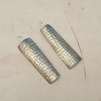 Boucles d'oreilles longues ethniques en argent massif martelé, légèrement asymétriques. Les reliefs, révélés par la patine, évoquent le tronc du "tucum", palmier tropical.