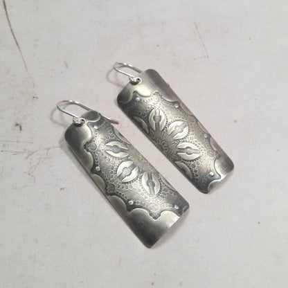 Boucles d'oreilles en argent massif au charme artisanal, patinées pour un effet vintage subtil. La délicate gravure d'une fleur ajoute une touche de romantisme à votre look. Une particularité remarquable réside dans les deux pièces qui, une fois unies, forment une seule fleur, symbolisant l'unité et la cohésion (Txai). La longueur est d'environ 5.3 cm.