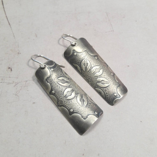 Boucles d'oreilles en argent massif au charme artisanal, patinées pour un effet vintage subtil. La délicate gravure d'une fleur ajoute une touche de romantisme à votre look. Une particularité remarquable réside dans les deux pièces qui, une fois unies, forment une seule fleur, symbolisant l'unité et la cohésion (Txai). La longueur est d'environ 5.3 cm.