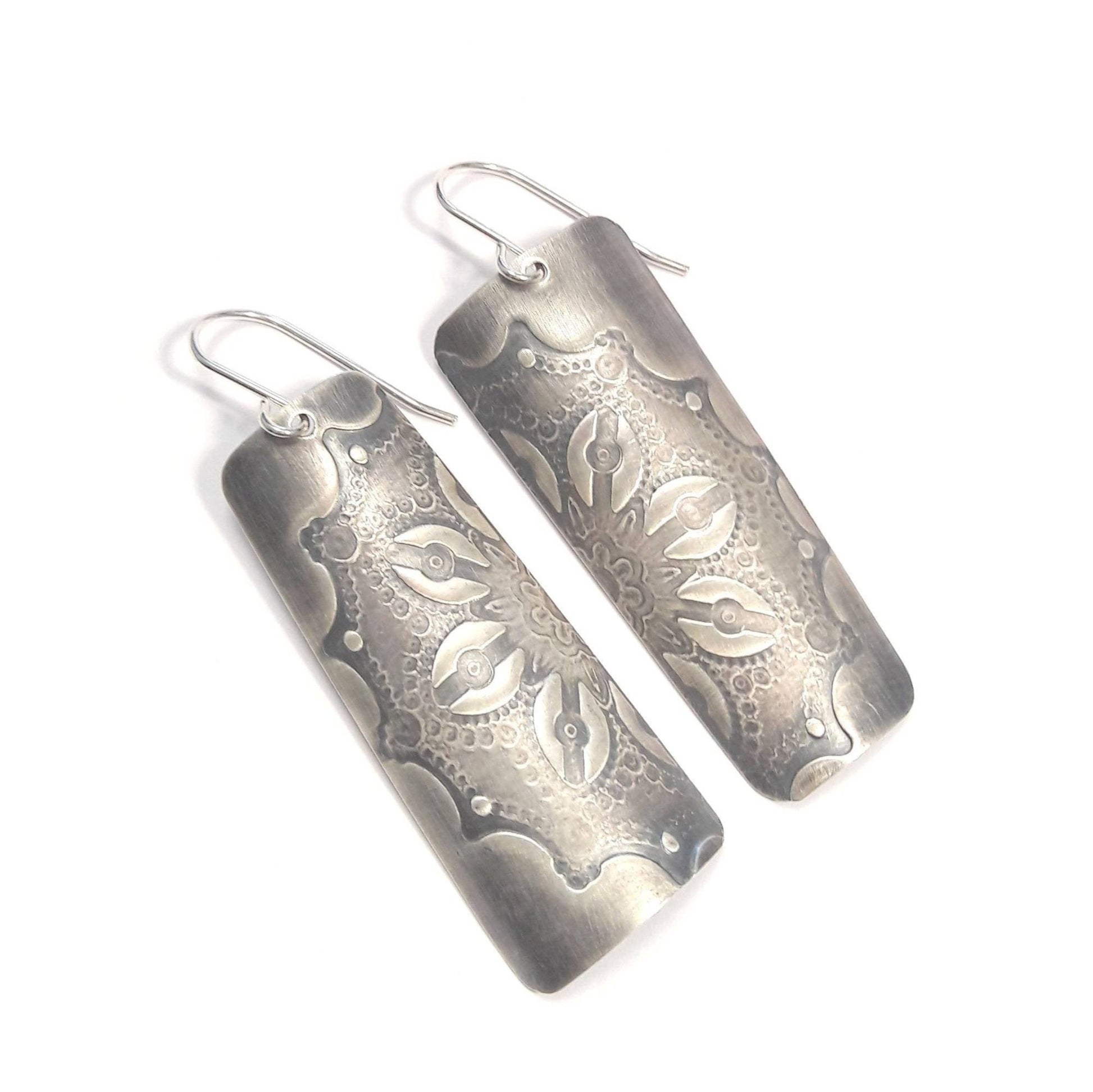 Boucles d'oreilles en argent massif au charme artisanal, patinées pour un effet vintage subtil. La délicate gravure d'une fleur ajoute une touche de romantisme à votre look. Une particularité remarquable réside dans les deux pièces qui, une fois unies, forment une seule fleur, symbolisant l'unité et la cohésion (Txai).  Boucles d'oreilles fleur.