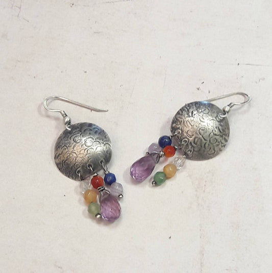 Les boucles d'oreilles ethniques en argent massif patiné et martelé sont ornées de pierres naturelles telles que l'améthyste, le lapis, le cristal de roche, l'aventurine, l'agate et la cornaline. Chaque bijou, façonné à la main, présente de petites différences par rapport au modèle photographié, ajoutant une touche unique à chaque pièce. Inspirée des vibrantes couleurs de Salvador, cette collection propose un voyage sensoriel célébrant l'expression de la joie de vivre.