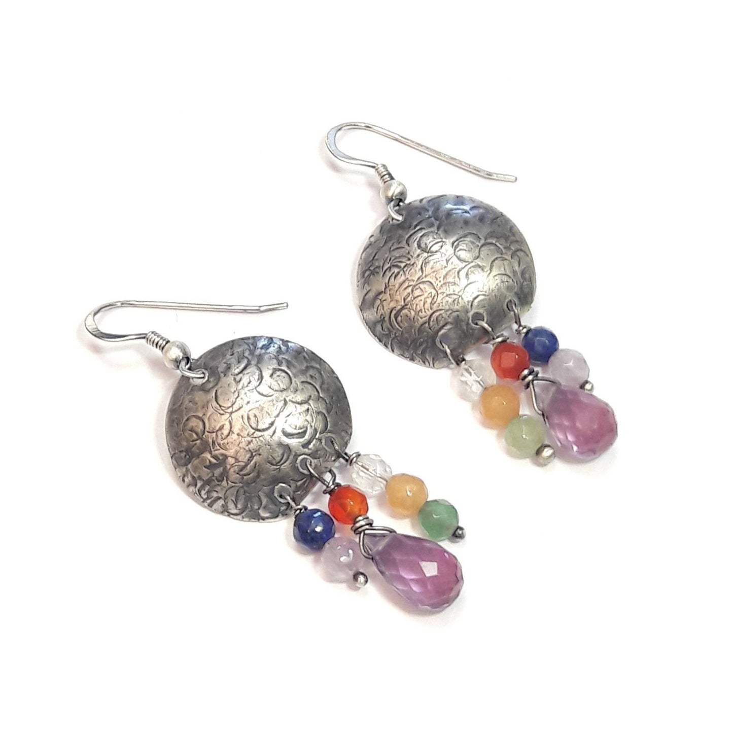 Les boucles d'oreilles ethniques en argent massif patiné et martelé sont ornées de pierres naturelles telles que l'améthyste, le lapis, le cristal de roche, l'aventurine, l'agate et la cornaline. Chaque bijou, façonné à la main, présente de petites différences par rapport au modèle photographié, ajoutant une touche unique à chaque pièce. Inspirée des vibrantes couleurs de Salvador, cette collection propose un voyage sensoriel célébrant l'expression de la joie de vivre.