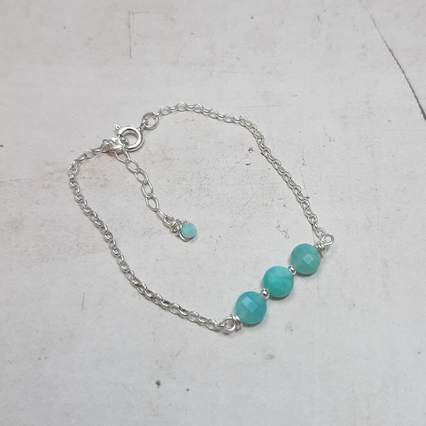 Ce bracelet raffiné mesure 16 cm, avec une chaînette pour un ajustement optimal. Fabriqué en argent 925, il est orné de pierres naturelles d'amazonite, dont les teintes peuvent varier légèrement, ajoutant une touche d'unicité à chaque pièce. L'amazonite est connue pour ses propriétés apaisantes, favorisant la joie de vivre et l'importance de l'instant présent. Ce bracelet constitue un choix idéal pour marquer des moments spéciaux ou pour apporter une note d'élégance au quotidien. 