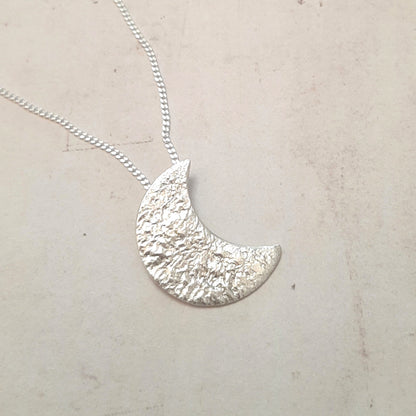 Collier avec un pendentif croissant de lune en argent massif réticulé.