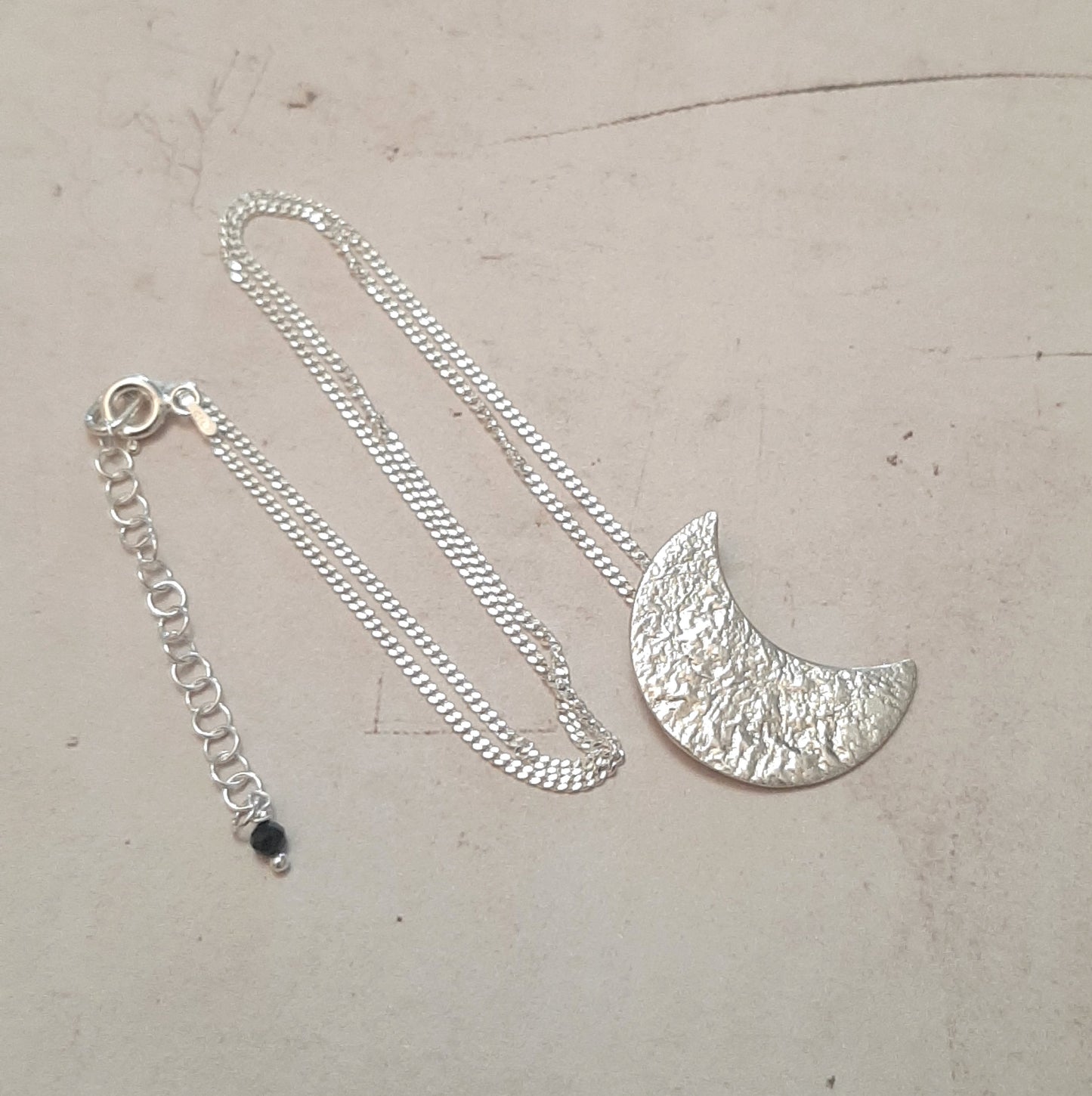 Collier chaine avec un pendentif croissant de lune en argent massif réticulé.