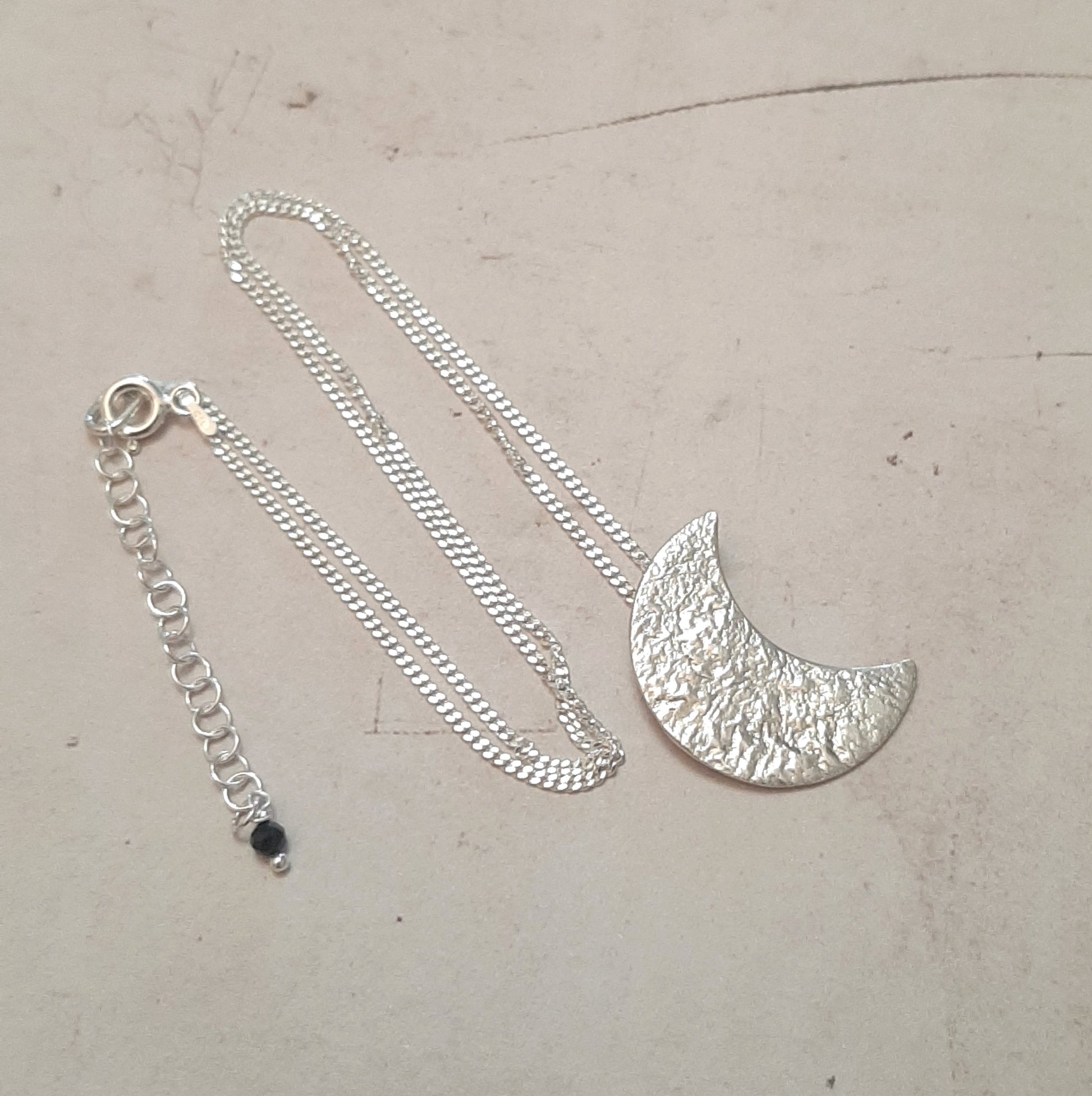 Collier chaine avec un pendentif croissant de lune en argent massif réticulé.