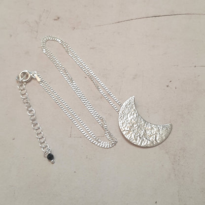 Collier chaine avec un pendentif croissant de lune en argent massif réticulé.