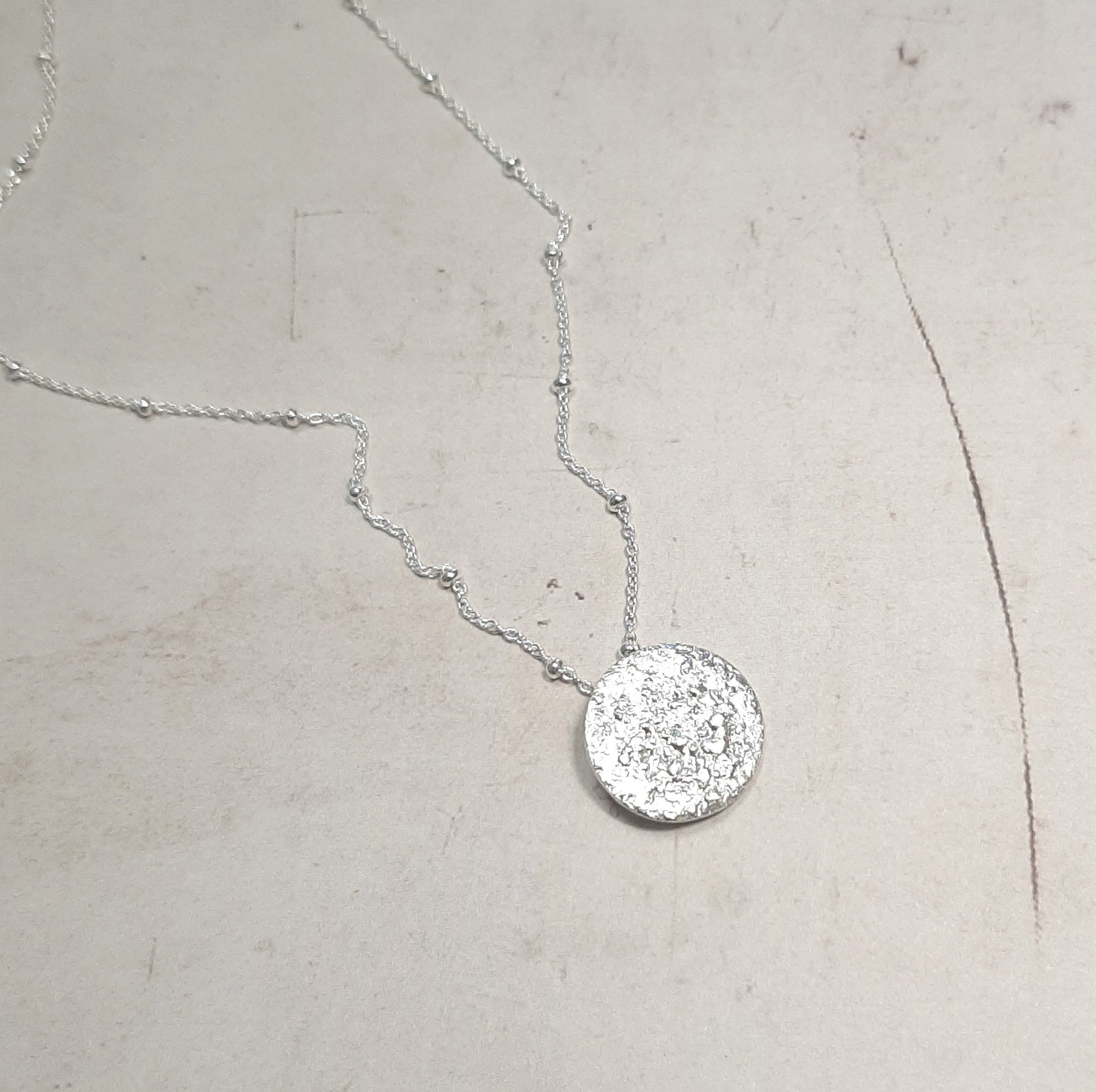 Le collier Jaci est inspiré par la pleine lune, symbole de féminité, d'intuition et de renouveau. La lune a été un guide spirituel pour de nombreuses civilisations, et ce bijou capture cette essence mystique. Réalisé en argent massif, il allie élégance et simplicité, faisant de ce collier un talisman unique. Idéal pour les amoureux de la nature et ceux cherchant des bijoux au sens profond, le collier Jaci est un choix éthique et artisanal.