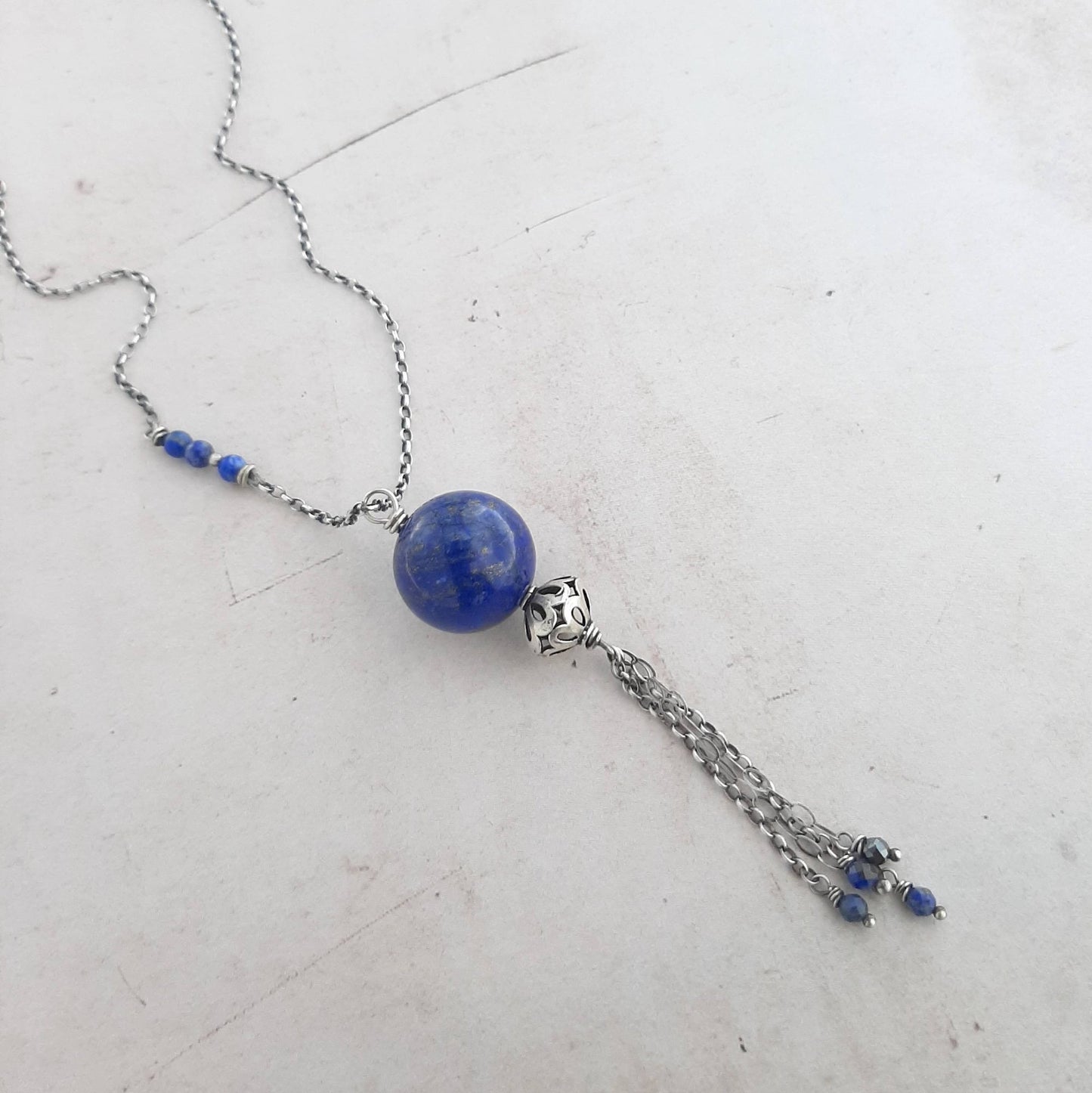 Ce bijou unique est un collier long, sans fermoir, réalisé en argent 925. Il est orné d'un pendentif en lapis-lazuli, une pierre naturelle bleue profonde. La longueur totale du collier est de 90 centimètres.