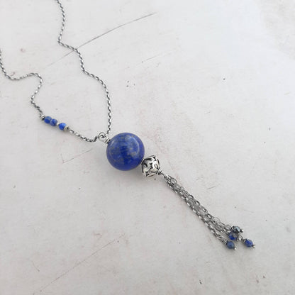Ce bijou unique est un collier long, sans fermoir, réalisé en argent 925. Il est orné d'un pendentif en lapis-lazuli, une pierre naturelle bleue profonde. La longueur totale du collier est de 90 centimètres.